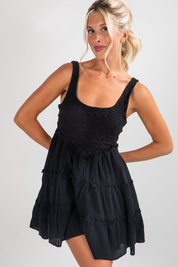 Woman wearing a black tiered dress against a plain background