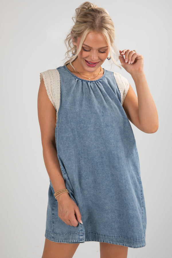 Woman wearing a denim dress with lace sleeves on a plain background